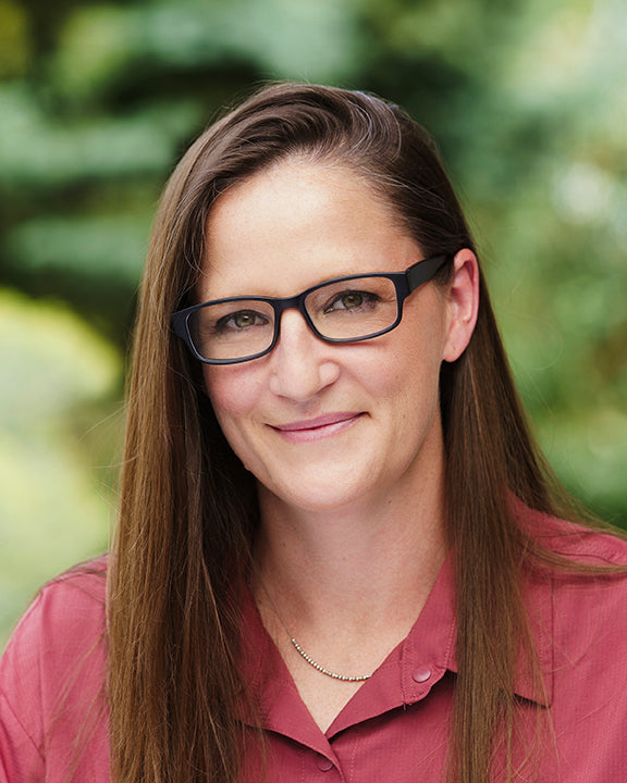 Brunette woman with black-rimmed glasses smiling outdoors
